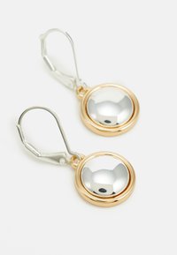 Boucles d'oreilles en métal doré et argenté avec une surface ronde, réfléchissante et polie ; fermeture à levier sécurisée ; texture lisse et finition brillante.