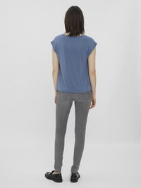 Avslappet blå t-skjorte med korte ermer kombinert med smale grå jeans, som har en jevn tekstur, og svarte slip-on sko med en polert overflate.