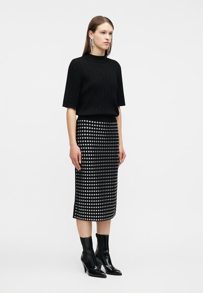 Γυναίκα που φοράει μαύρο ριμπ κοντομάνικο τοπ, μαύρη μίντι φούστα με ασημένιο μοτίβο με οπές, μακριά κρυστάλλινα σκουλαρίκια και μαύρα μποτάκια με τακούνι.