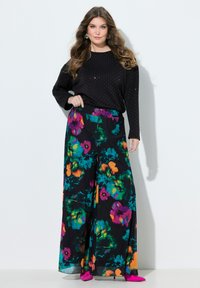 Černý top s dlouhým rukávem se stříbrnými puntíky, doplněný barevnými širokými kalhotami s květinovým vzorem. Outfit doplňují růžové boty se špičatou špičkou.