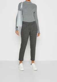 Grijze geribbelde coltrui, op maat gemaakte broek met ruitpatroon in donkergrijs en zwart, witte sneakers en een lichtblauwe handtas.