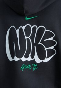 Černá mikina s kapucí, která má výrazný bílý graffiti styl "NIKE" text a zelenou výšivku "SINCE '72". Malé zelené logo Nike v horním rohu.