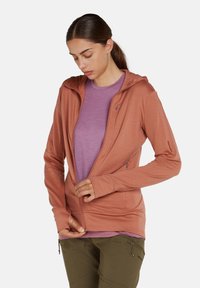 Felpa con zip color ruggine dalla texture morbida, dotata di cappuccio, maniche lunghe e vestibilità slim, indossata sopra una maglietta viola chiaro.