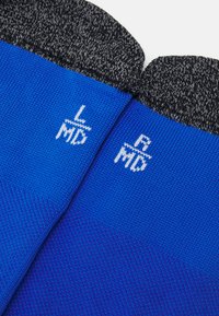 Kék zoknik struktúrált anyagból, szürke melírozott díszítéssel a tetején. Fehér méretcímkék "L/MD" és "R/MD" láthatók.