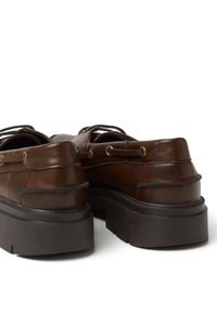 Scarpe in pelle marrone con suola nera spessa, dotate di lacci con occhielli dorati e dettagli di cucitura stratificata sulla parte superiore.