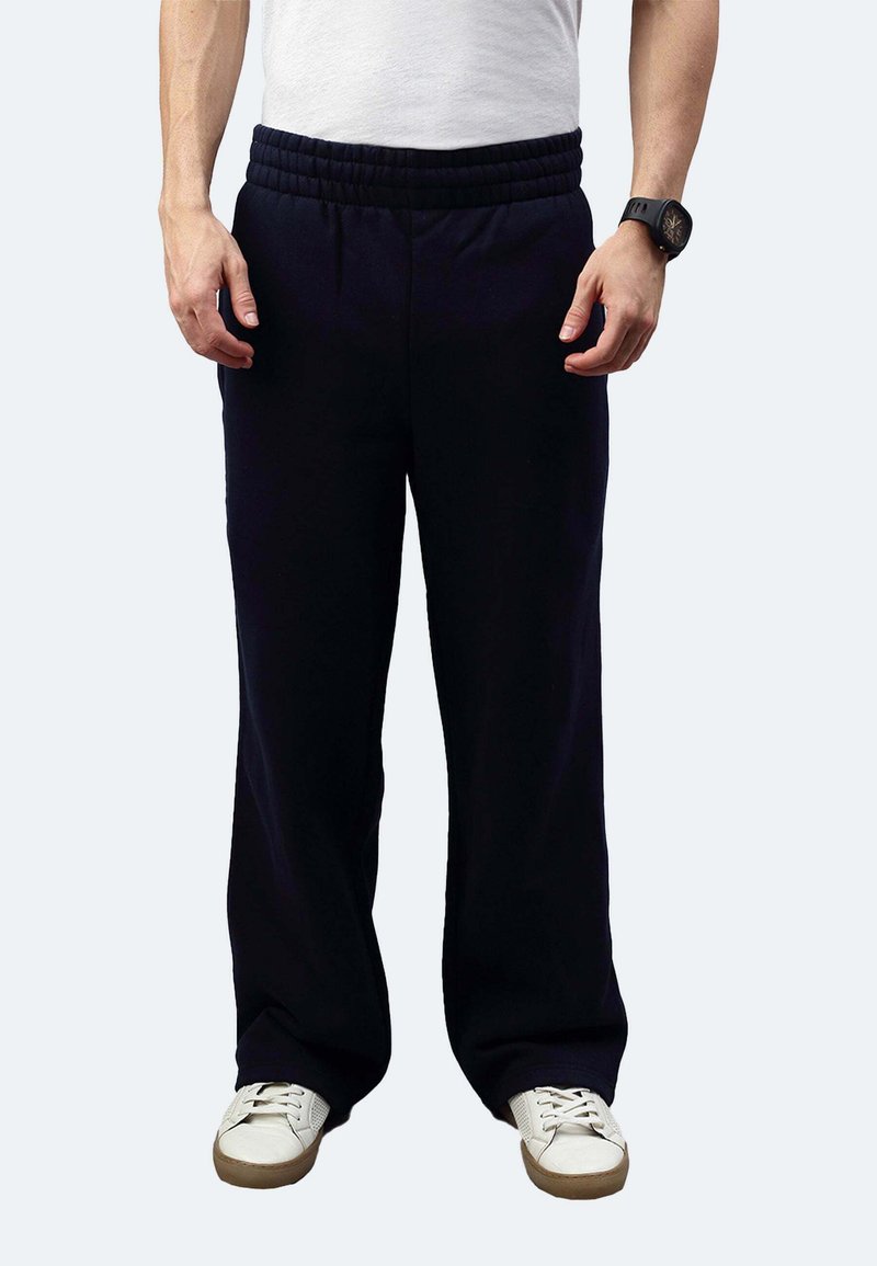 Marineblaue Jogginghose mit elastischem Bund, entspannter Passform und Seitentaschen, kombiniert mit weißen Sneakers auf hellem Hintergrund.