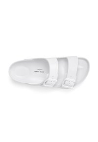 White slide sandal with two wide straps, each featuring adjustable buckles. Smooth texture with a contoured footbed. Brand logo printed on insole.