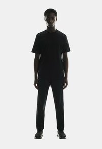 Black short-sleeve t-shirt paired with black trousers and black sneakers. The outfit features a simple design and a sleek, minimalist look.