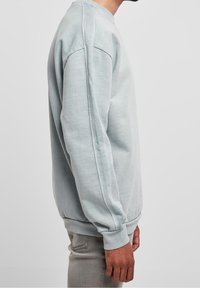 Světle modrá mikina vyrobená z měkké tkaniny, s kulatým výstřihem, žebrovanými manžetami a lemem, a uvolněným střihem se vsazenými rukávy.