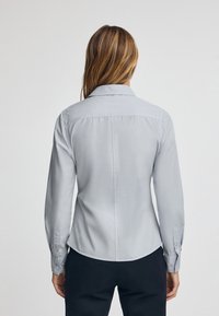 Ljust grå långärmad skjorta med knappar, klassisk krage, figursydd design och enfingerknappar. Slät tyg med ryggsömm.