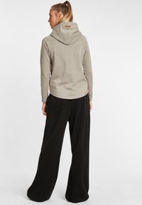 Ljusgrå hoodie med ett texturerat mönster, har en stor huva och en liten logotyp på ryggen. Matchad med svarta byxor med vida ben.