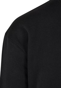 Suéter de algodón negro con una textura suave, costura de hombro redondeada y un diseño minimalista sin patrones o acentos visibles.