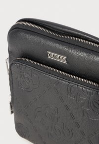 Schwarze Taschen aus Kunstleder mit geprägtem Logo-Muster, silbernen Beschlägen, einem oberen Reißverschluss und einer vorderen Reißverschlusstasche. Die strukturierte Oberfläche erhöht die Langlebigkeit.