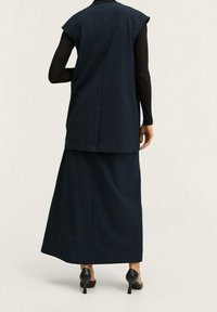 Completo due pezzi navy composto da un gilet lungo a maniche corte e una gonna lunga coordinata, realizzato in tessuto testurizzato, abbinato a tacchi neri.