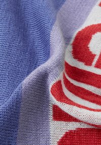 Knitted fabric in lavender and light purple with a bold red and white geometric pattern. Textured surface with prominent color contrast.