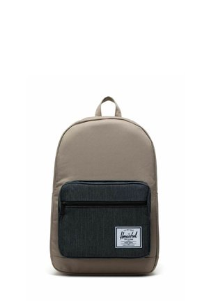 Sac à dos en tissu beige avec une poche avant gris foncé, doté d'une fermeture éclair, d'une poignée supérieure en boucle et d'un patch blanc avec le logo.