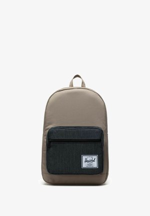 Sac à dos en tissu beige avec une poche avant gris foncé, doté d'une fermeture éclair, d'une poignée supérieure en boucle et d'un patch blanc avec le logo.