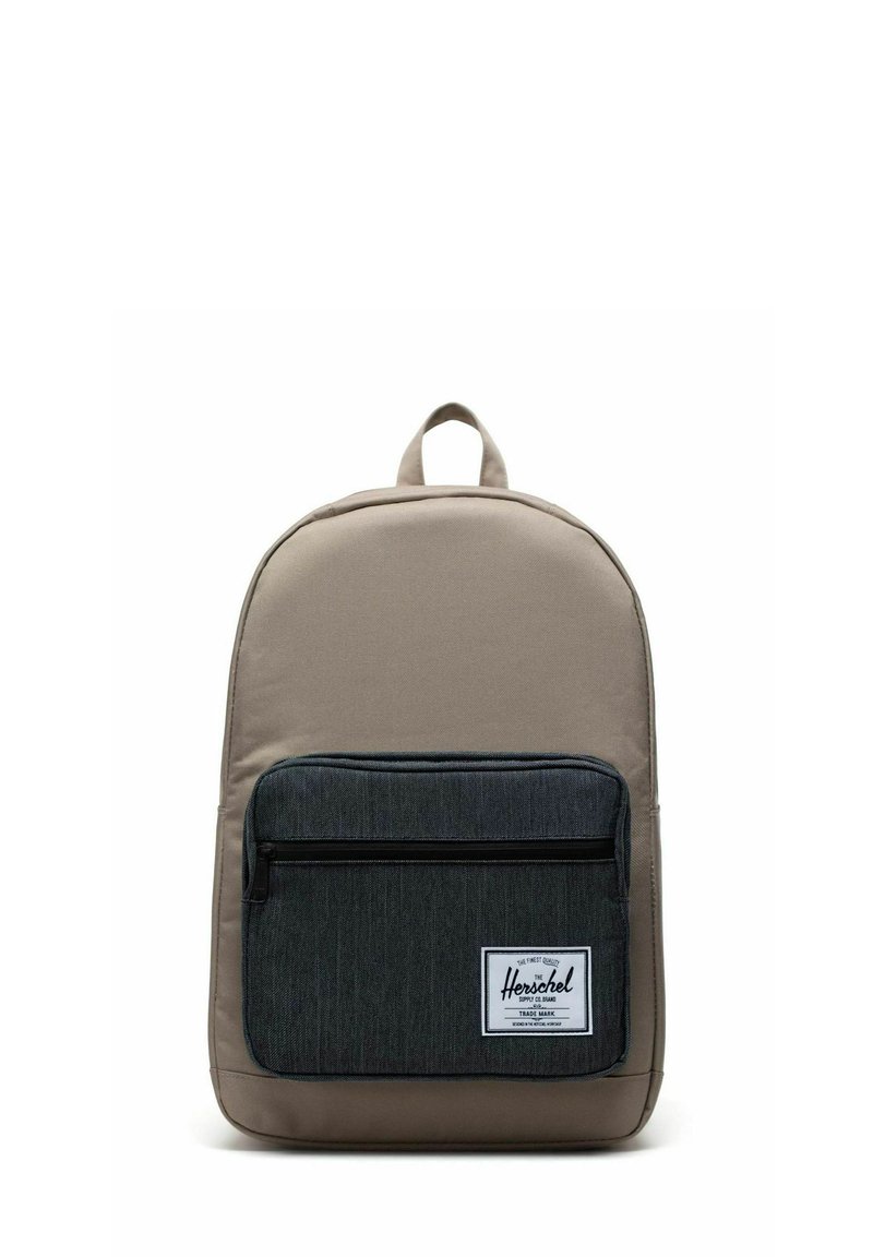 Sac à dos en tissu beige avec une poche avant gris foncé, doté d'une fermeture éclair, d'une poignée supérieure en boucle et d'un patch blanc avec le logo.