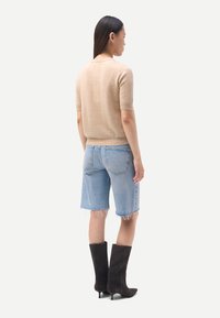 Haut beige à manches courtes en tricot, short en jean bleu clair avec ourlets effilochés, et bottes noires à talons montant jusqu'aux genoux. Design simple et épuré.