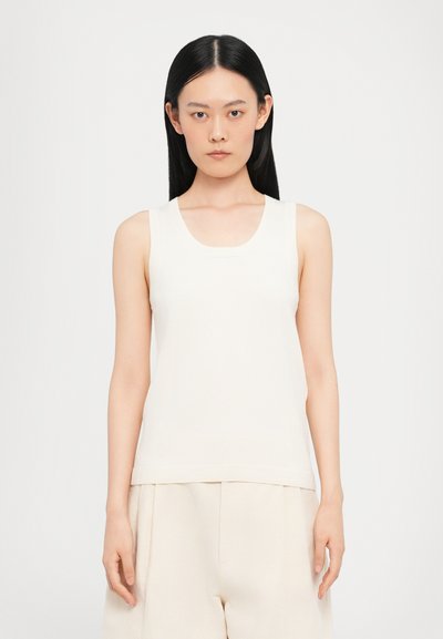 Haut sans manches couleur crème avec un col rond, des bords côtelés et une texture lisse, associé à un pantalon ample beige clair.