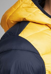 Yellow and navy puffer jacket section showing quilted design, contrasting colors, and smooth texture, with a hood and stitched detailing.