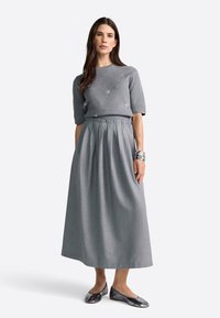 Pelēks adīts džemperis ar īsām piedurknēm, kas rotāts ar nelielām embellishments, saskaņots ar garu pelēku svārku. Modelis valkā spīdīgas pelēkas kurpes.