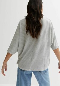 Top grigio chiaro a costine con una vestibilità rilassata, spalle scese e maniche corte, abbinato a jeans blu a vita alta.