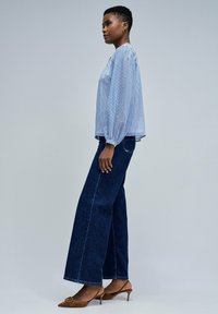 Hellbluse mit Streifen und Puffärmeln, kombiniert mit dunkelblauen weit geschnittenen Jeans und braunen spitzen High Heels.