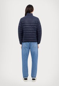 Navy puffer jacket with a high collar and quilted design, paired with light blue loose-fit jeans and black-accented white shoes.