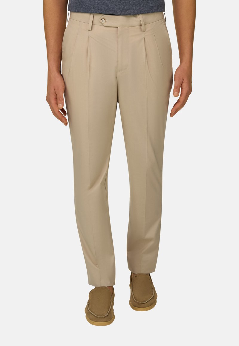 Homme portant un pantalon plissé beige et des mocassins en daim marron, debout les mains détendues le long du corps.