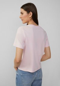 Helles rosa T-Shirt mit kurzen Ärmeln und rundem Ausschnitt. Weiches Baumwollmaterial, lockere Passform und ein leicht verkürzter Saum. Kombiniert mit blauen Jeans.