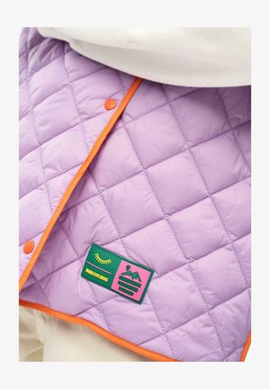 Fioletowa pikowana tkanina z pomarańczową lamówką i zatrzaskami, z zielono-różową naszywką z napisem „Mango Explorers” oraz grafiką gór.