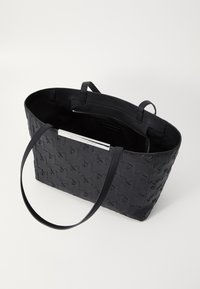 Borsa tote nera realizzata in materiale intrecciato con texture liscia. Presenta due manici e una tasca interna con zip, mostrando un design minimalista.