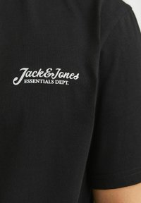 Camiseta negra de manga corta hecha de algodón, con un logo impreso en blanco que dice "Jack & Jones ESSENTIALS DEPT." en la parte superior de la espalda.