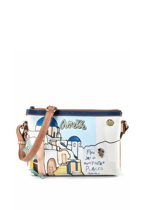 Kleine Umhängetasche mit weißen Gebäuden im Santorini-Stil und blauen Kuppeln, braunem Riemen und dem Text "Finde Freude an unerwarteten Orten."