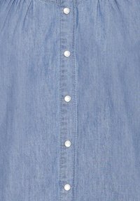 Lichtblauw denimshirt met een knoopsluiting aan de voorkant, voorzien van witte plastic knopen en een licht gestructureerde stof. Subtiele plooitjes bij de schouders.