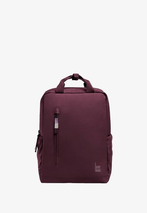 Mochila marrón con un acabado suave, que cuenta con un asa superior, un bolsillo frontal con cremallera y un bolsillo de malla en el lado. Logotipo impreso en la parte inferior derecha.