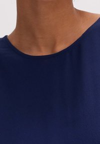 Granatowa bluzka z okrągłym dekoltem i gładką teksturą. Materiał wydaje się lekki i ma delikatny połysk.