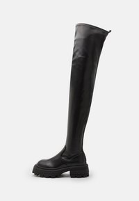 Botas de cuero negro hasta la rodilla con un diseño elegante, acabado texturizado, suela de goma gruesa y detalles de costura mínimos.