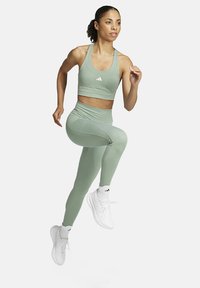 Lichtgroene sportieve crop top en leggings van rekbaar materiaal, gecombineerd met witte hardloopschoenen en enkelkousen.