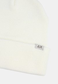 Berretto lavorato a maglia bianco con una texture a coste. Presenta un piccolo etichetta con un logo grigio. Materiale morbido e design semplice, adatto per un abbigliamento casual.