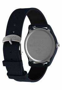 Montre solaire Timex avec un bracelet en tissu bleu marine, un dos en acier inoxydable et un boîtier rond. Dispose d'une boucle en argent et de détails gravés.