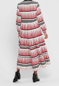 Robe maxi à motifs rouges et blancs avec des accents noirs, manches longues et couches à volants, accompagnée de bottines.