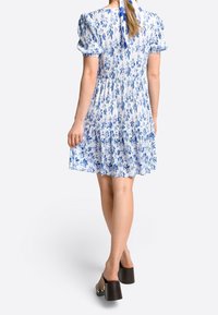 Vestido floral azul y blanco con mangas cortas abullonadas, falda en capas y un lazo en la parte posterior, combinado con zuecos oscuros de plataforma.