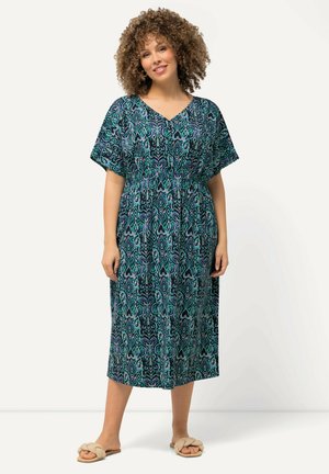 Maxikleid mit einem blauen und grünen Musterdesign, kurzen Ärmeln, V-Ausschnitt und einem elastischen Taillenbund für eine optimale Passform. Kombiniert mit beigen Sandalen.