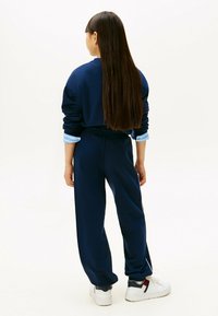 Marineblauwe trainingsoutfit met een ontspannen pasvorm. Lange mouwen met opgerolde manchetten, een elastische tailleband op de broek en klassieke witte sneakers.