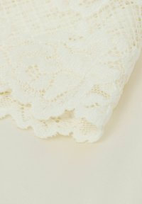 Vitt spetstyg med intrikata blommönster och vågiga kanter, som visar en ömtålig, texturerad design. Mjukt, lätt material.