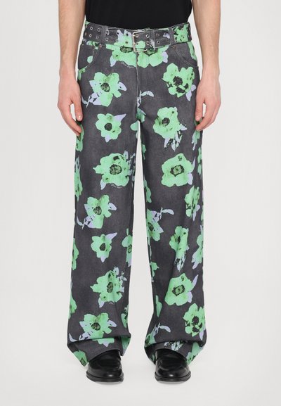 Jeans larghi in tessuto nero con grandi motivi floreali verdi e lavanda, completati da una cintura nera con fibbia argentata.