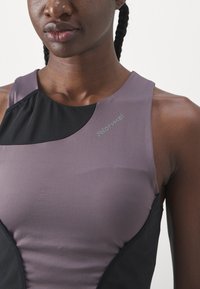 Modisches Sport-Top mit einem lavendelfarbenen Vorderteil, schwarzen Akzenten und einem hohen Kragen. Verfügt über ein Logo auf der Schulter. Glatte Stoffstruktur.