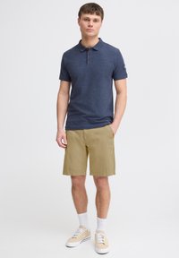 Marineblauwe polo met een drieknops-overslag, kaki shorts en beige sneakers; witte crew sokken; casual ontwerp met textuurstof.